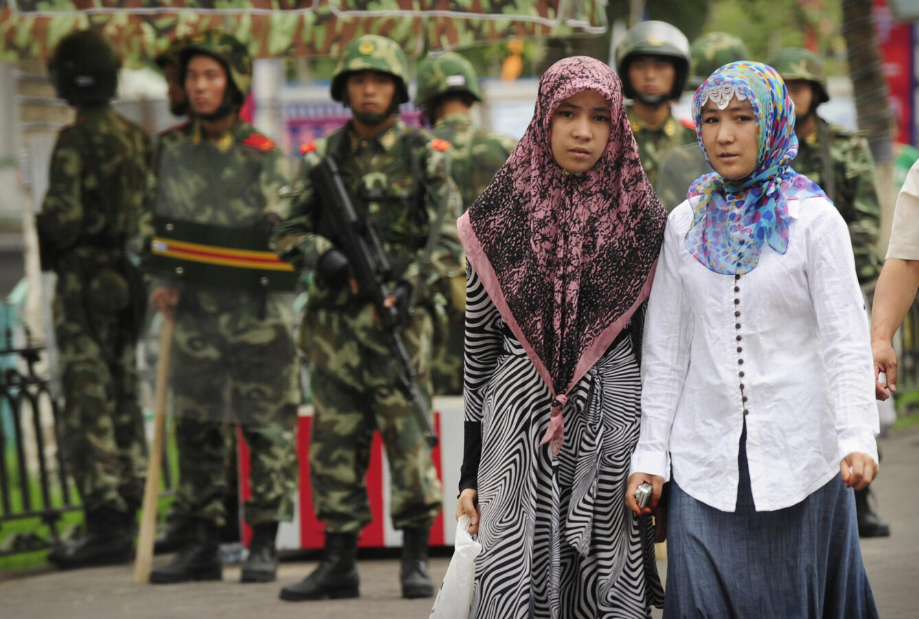 two ethnic uighur women pass chinese paramilitary policemen