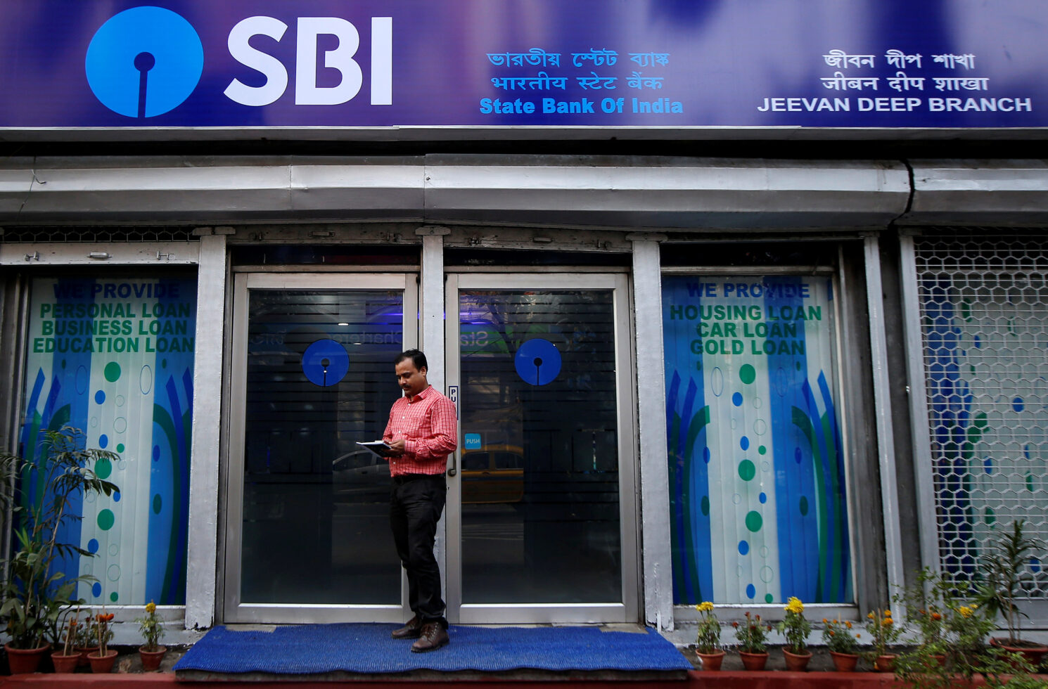 a man checks his mobile phones in front of state bank of india (sbi) branch in kolkata